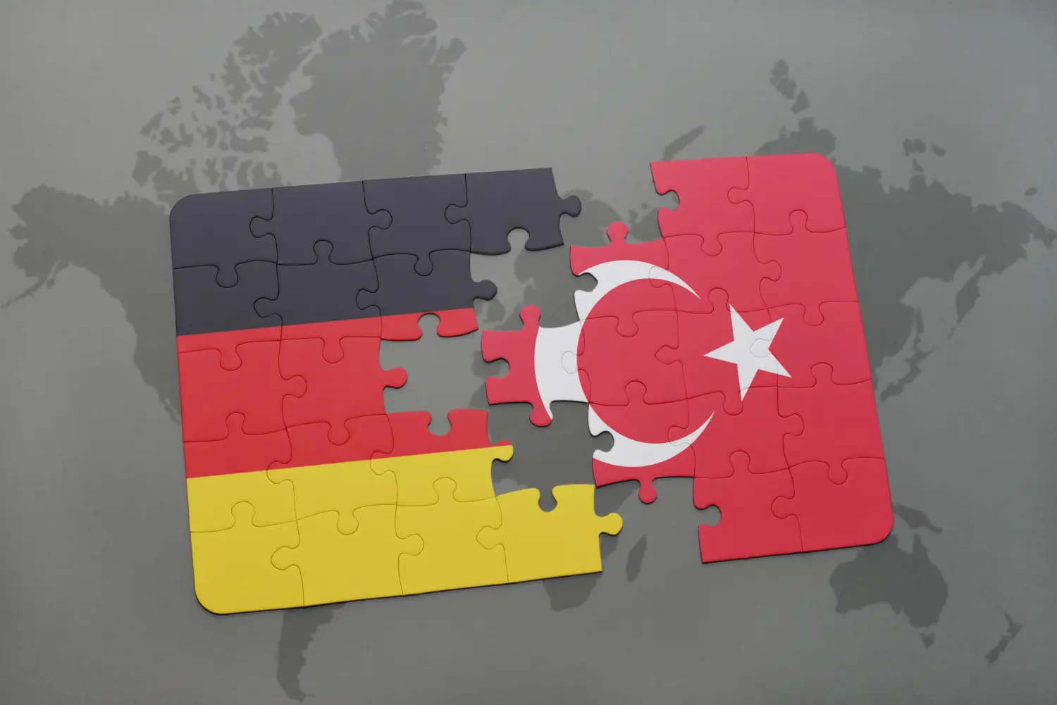 Puzzle mit der Nationalflagge von Deutschland und der Türkei auf einem Weltkartenhintergrund.