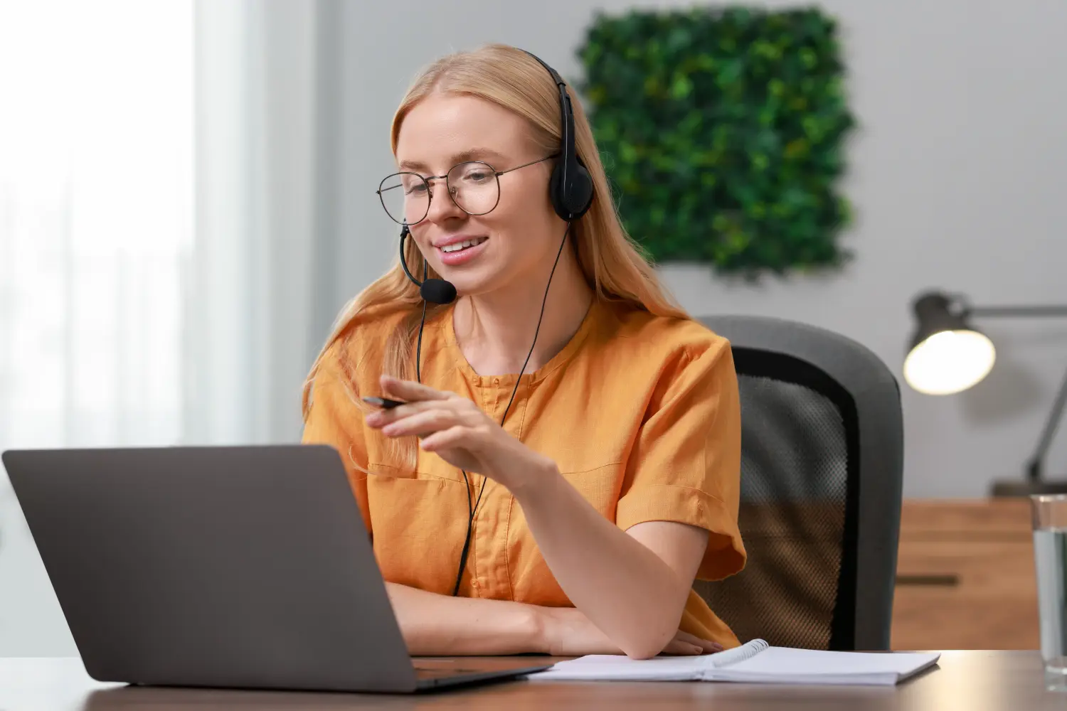 Dolmetscherin mit Headset führt Videochat über Laptop an einem Tisch im Innenbereich.